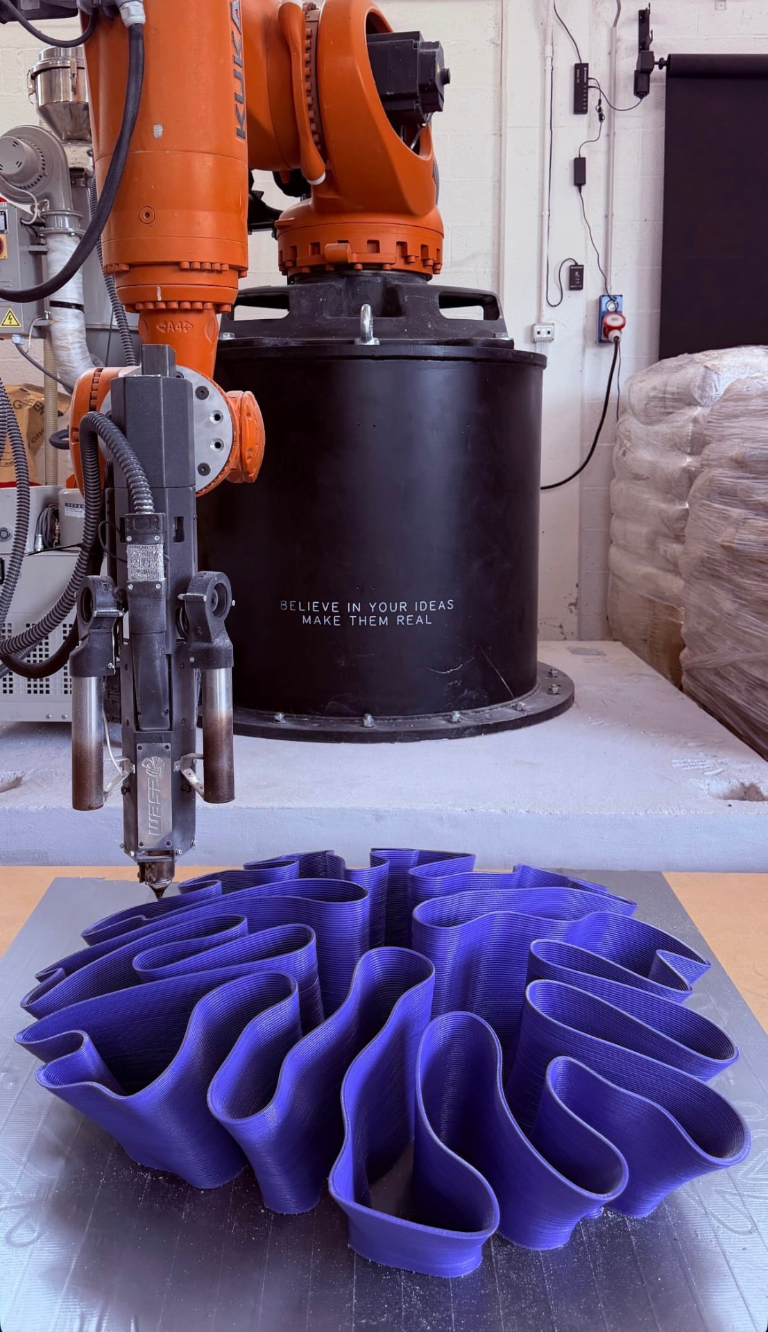 Orange robotic arm printing a large purple pleated vessel on a print bed