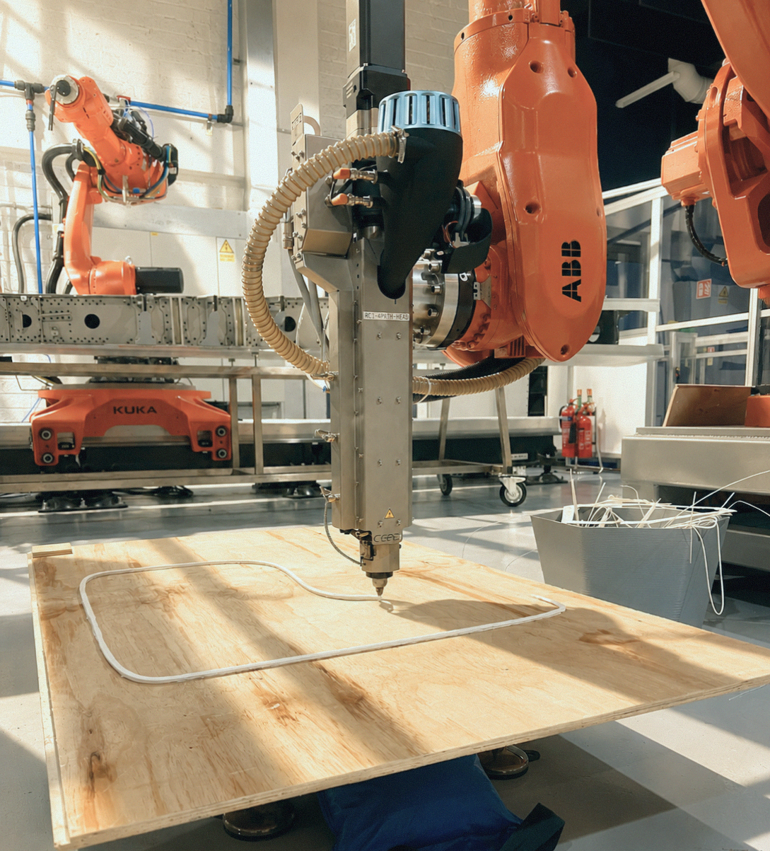 Orange robotic arm printing a large-format object on plywood in the Zerolab workshop